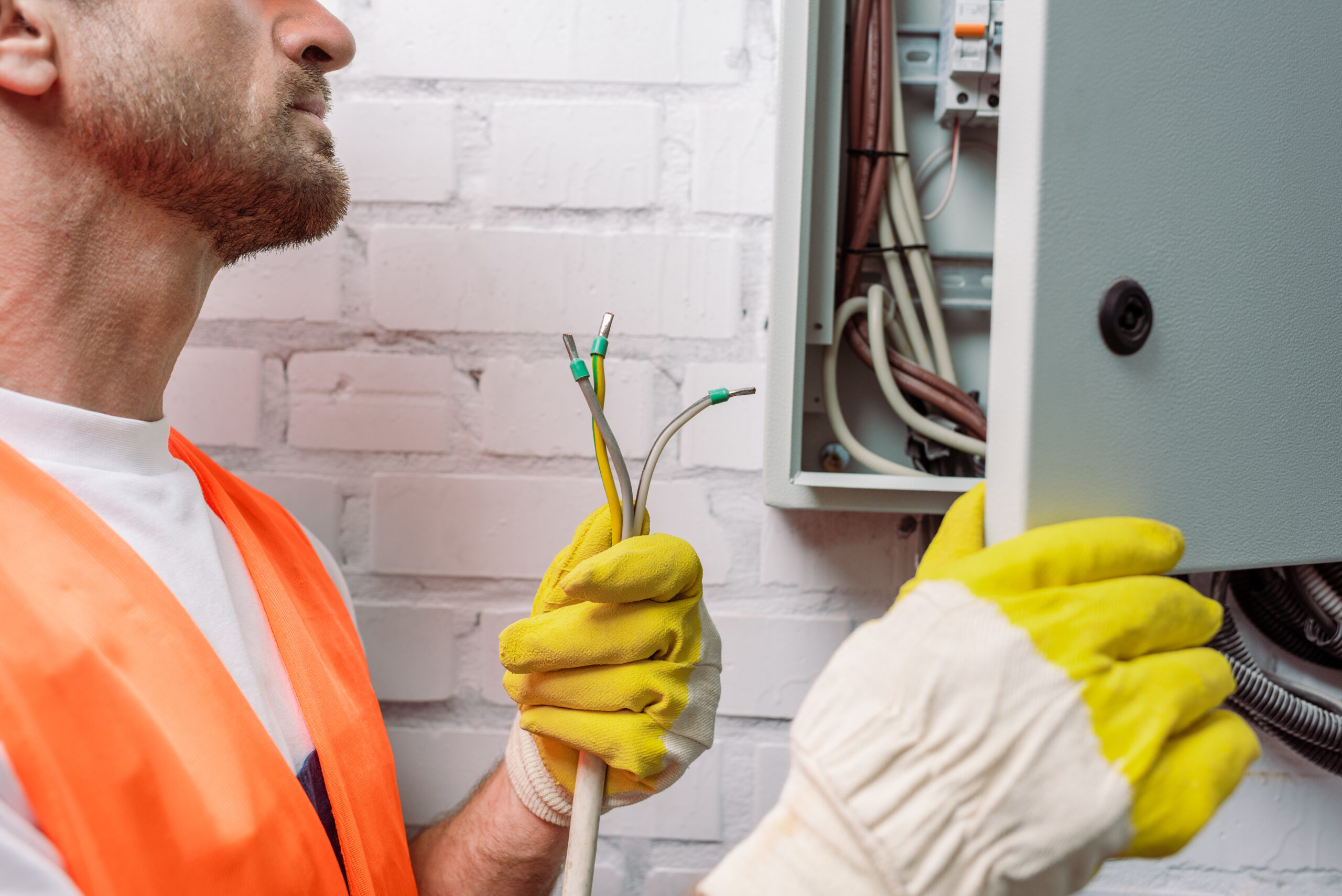 Cropped view of electrician in gloves holding wires near electrical distribution box Cropped view of electrician in gloves holding wires near electrical distribution box